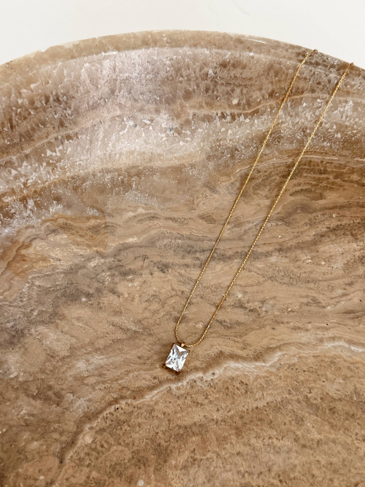 Gold necklace with a diamond pendant on a textured stone surface